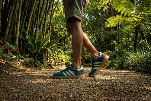 Person walking on a path in a forest wearing green Adidas Handball Spezial Shoes.