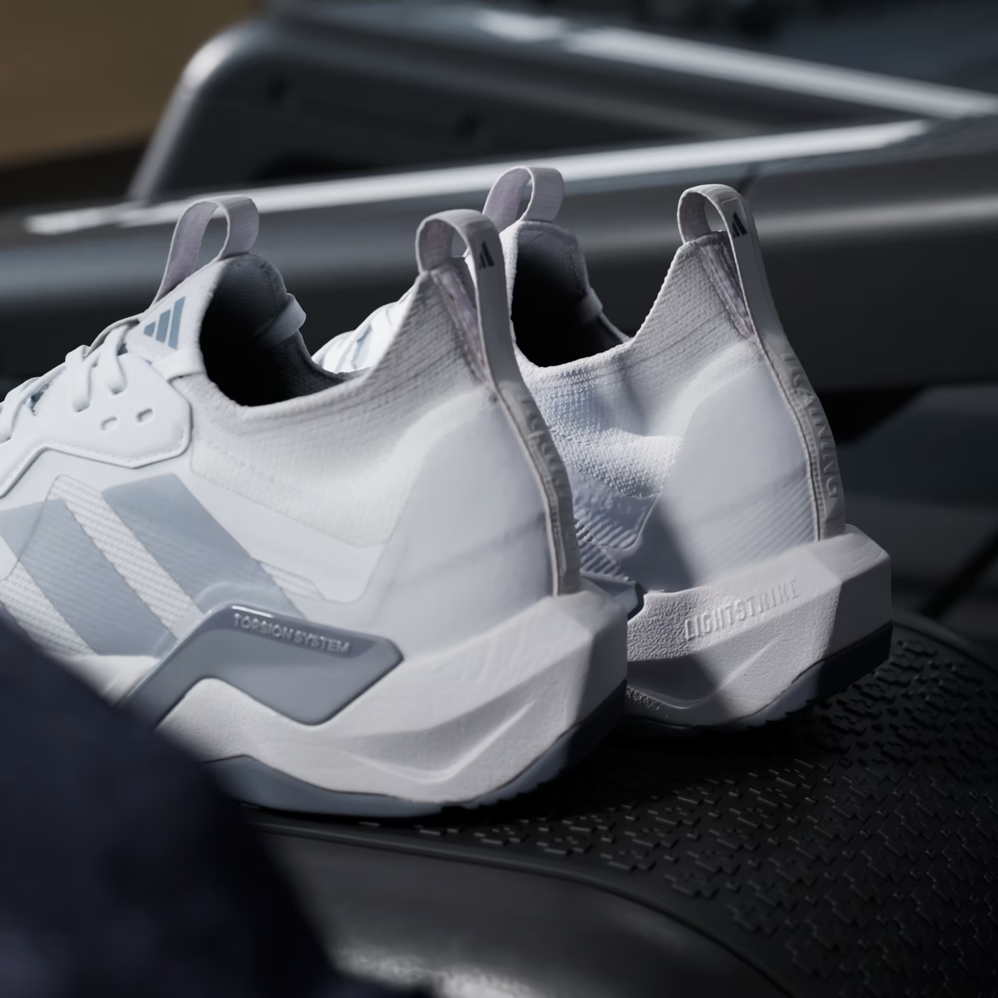 Adidas Rapidmove ADV 2 JI4196 - Lateral Midsole Close-up on Gym Floor showing Torsion System Embossed Panel, Lightstrike Pro Midsole Text, Grey Structural Overlays, Halo Silver Three Stripes & White Outsole Traction
