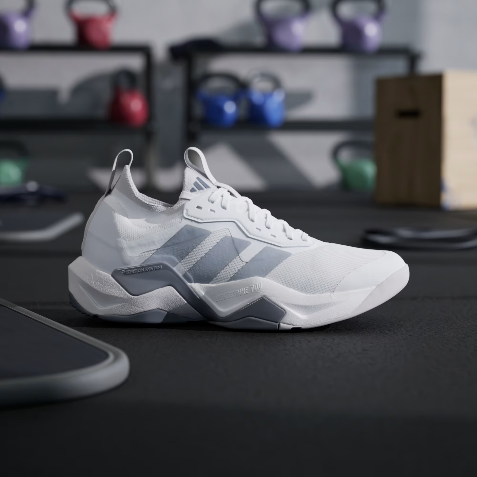 Adidas Rapidmove ADV 2 JI4196 - Front 3/4 Pair Shot on Gym Equipment in Cloud White/Halo Silver showing Engineered Mesh Upper, Halo Silver Three Stripes, Grey Structural Overlays & White Lightstrike Pro Midsole