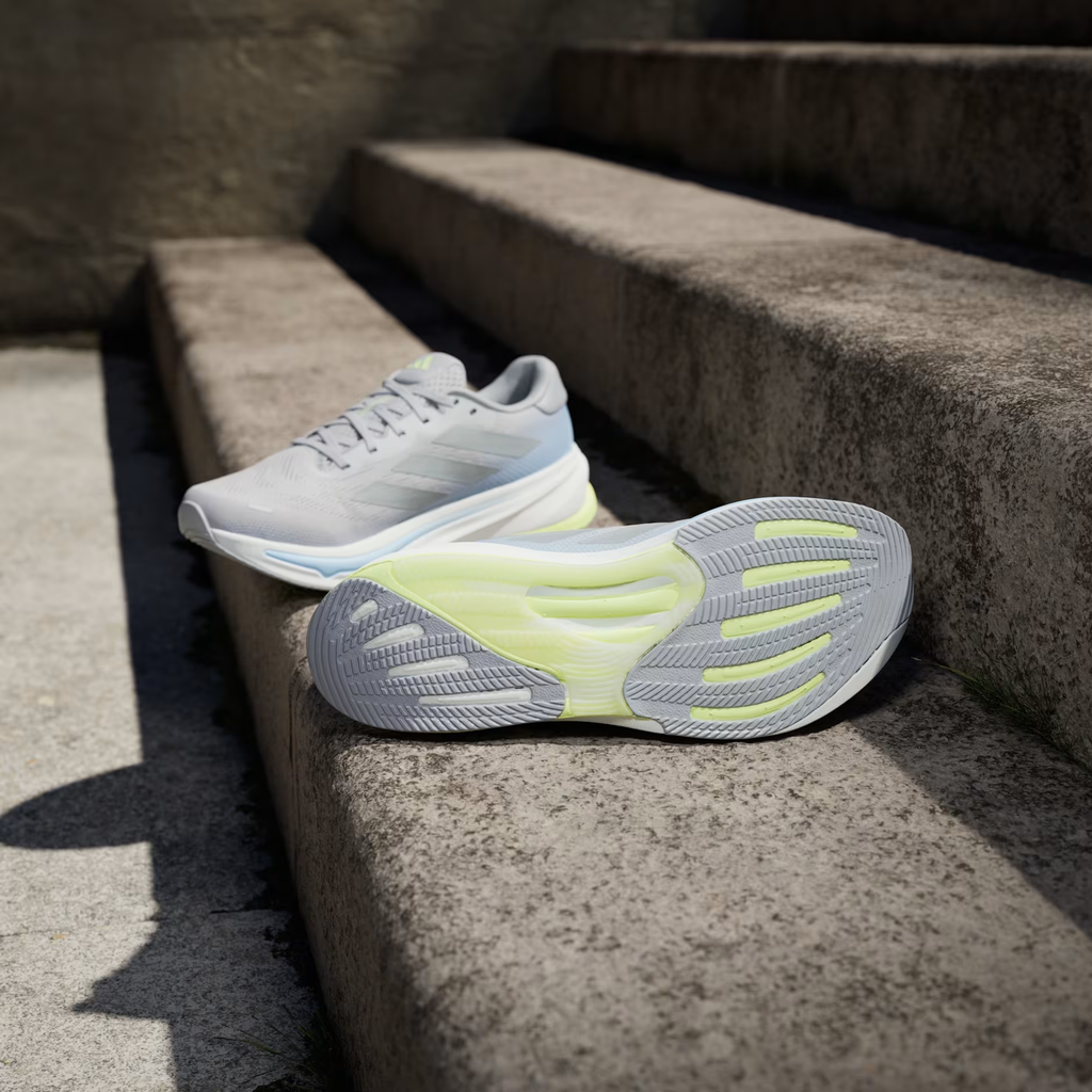 Adidas Supernova Rise 2 IH8708 - Rear Pair Shot on Stone Ledge with Blue Sky Background showing Grey Two Mesh Upper, Hi-Res Yellow Adidas Badge on Heel, Light Blue Collar Lining, White Dreamstrike+ Midsole & Hi-Res Yellow Bounce Outsole