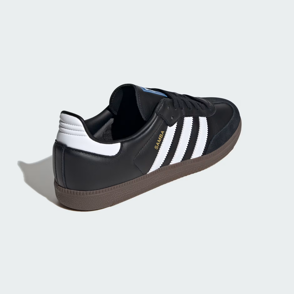 Adidas Samba OG B75807 - Lateral Midfoot & Heel Close-up showing Core Black Full-Grain Leather Texture, Gold Samba Wordmark, Cloud White Three Stripes Base, Cloud White Heel Tab, Blue Adidas Originals Trefoil Tongue Badge & Gum Rubber Outsole Edge