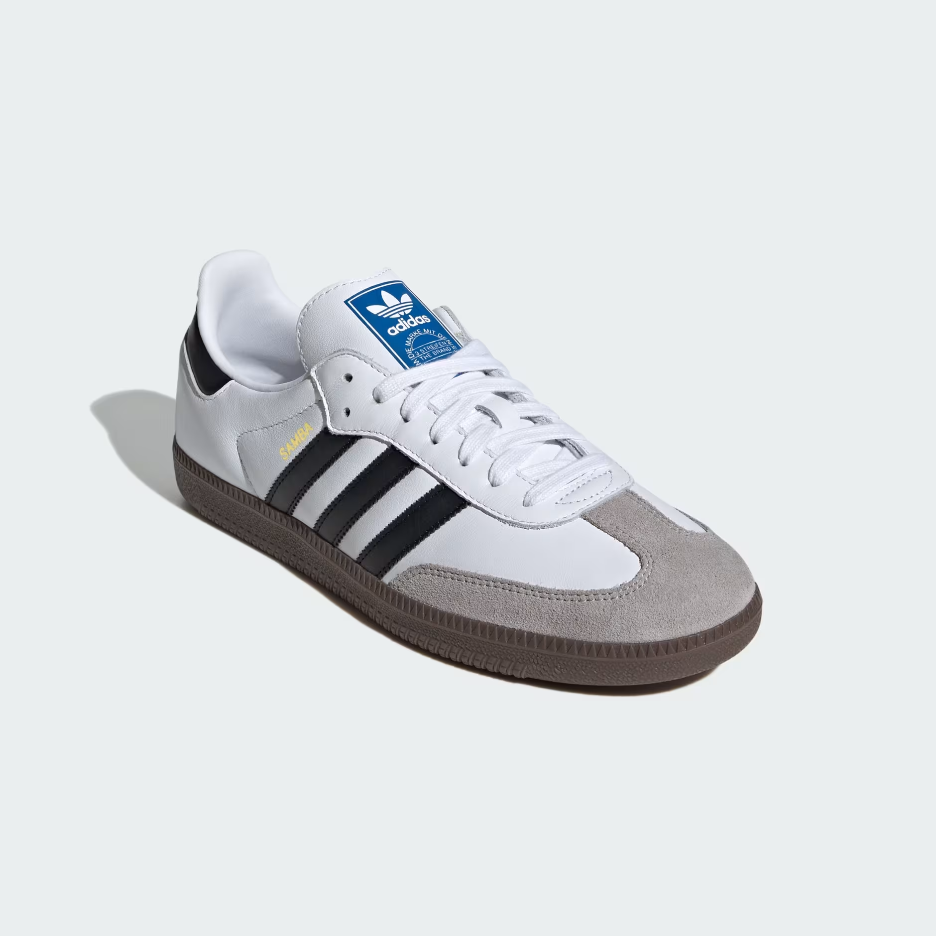 Adidas Samba OG B75806 - Lateral Profile Lifestyle Shot on Light Grey Background with Loose White Laces showing Cloud White Leather Upper, Gold Samba Wordmark, Core Black Three Stripes, Clear Granite Suede Toe Box, Blue Adidas Trefoil Tongue Badge & Gum Rubber Outsole