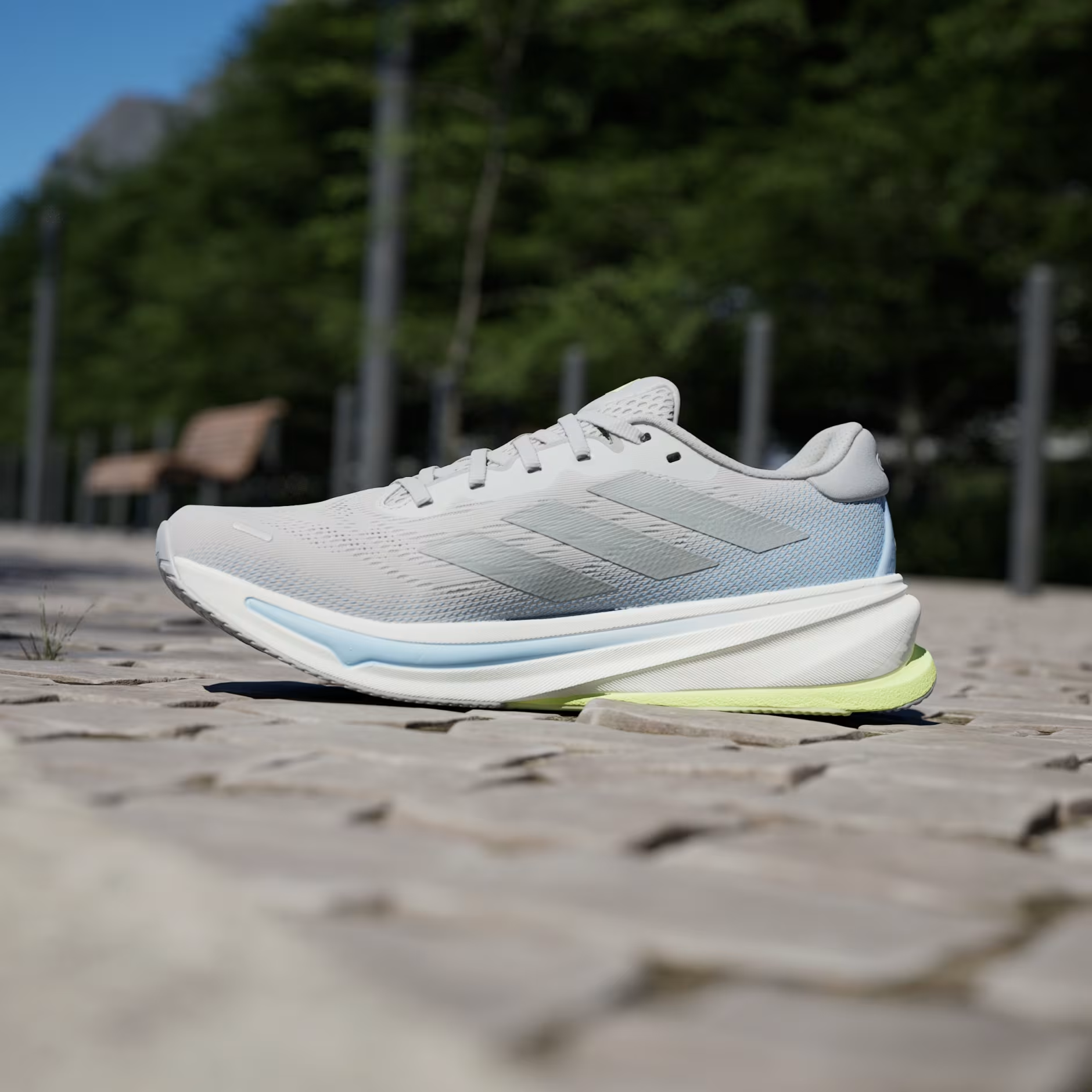 Adidas Supernova Rise 2 IH8708 - Low Angle Lateral Pair Shot on Stone Ledge showing Grey Two Mesh Upper, Tonal Matte Silver Three Stripes, Dreamstrike+ Midsole Text, Light Blue Midsole Stripe & Hi-Res Yellow Bounce Outsole