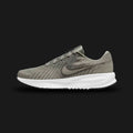 Nike Run Defy shoes in Light Army, Iron Grey, White, and Black (HM9594-300). Features a breathable engineered mesh upper, structured midfoot support overlays, a cushioned foam midsole, and a high-traction rubber outsole. Luxuntique guarantees 100% authentic footwear.
